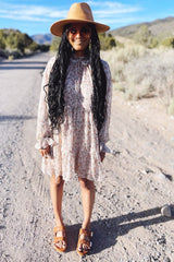 woman wearing a pink floral long sleeve dress with a ruffled hem, brown hat, and brown sandals, standing outdoors