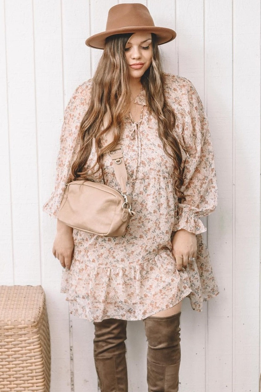 woman wearing a floral print long sleeve dress with a ruffled hem, styled with a brown hat and a beige crossbody bag