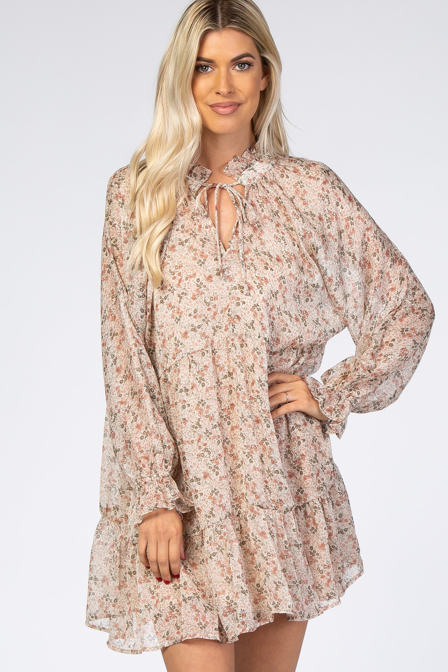 woman wearing a flowy floral print long sleeve dress with a tie neckline and ruffled hem