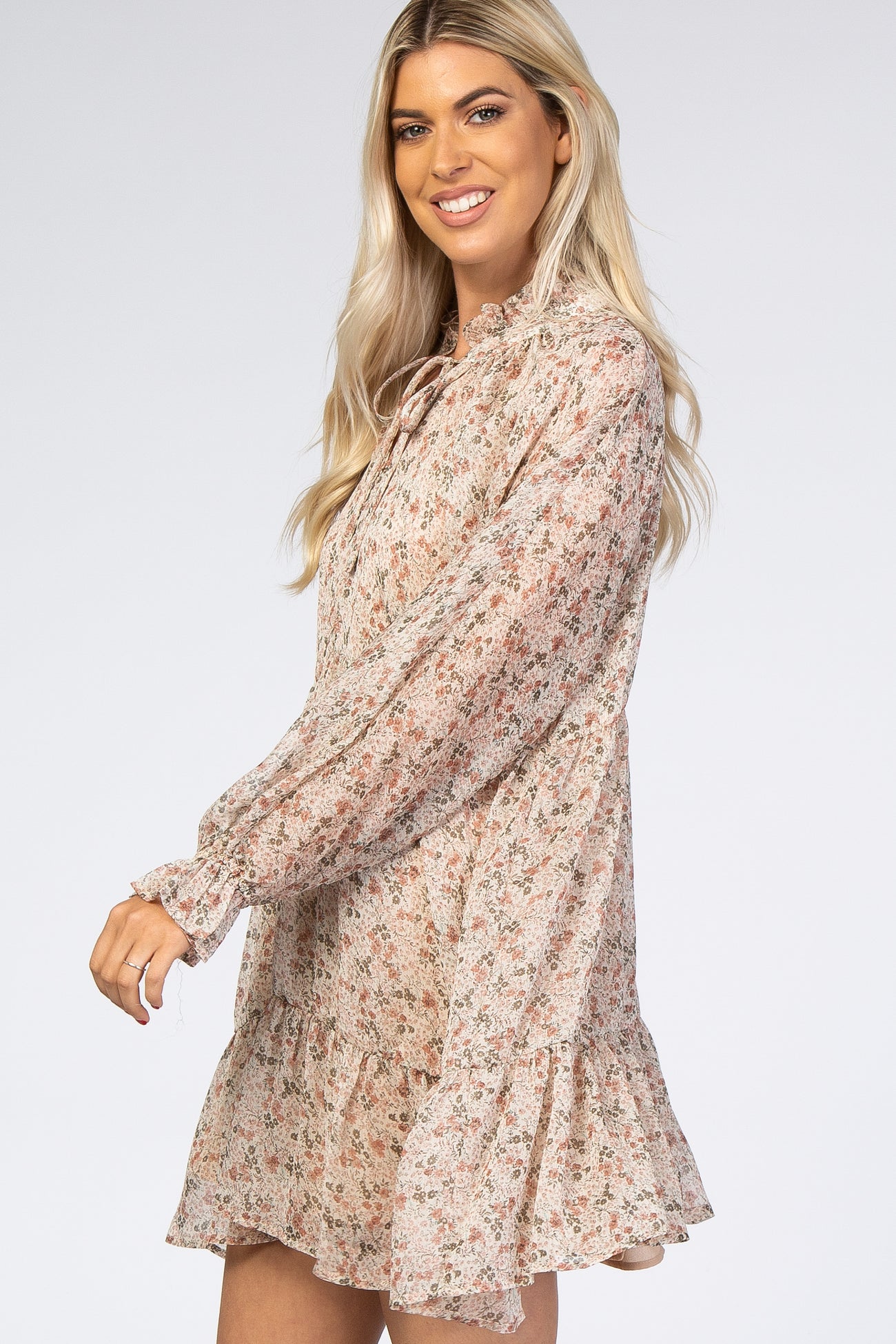 woman wearing a floral long sleeve mini dress with ruffled hem and tie neck detail