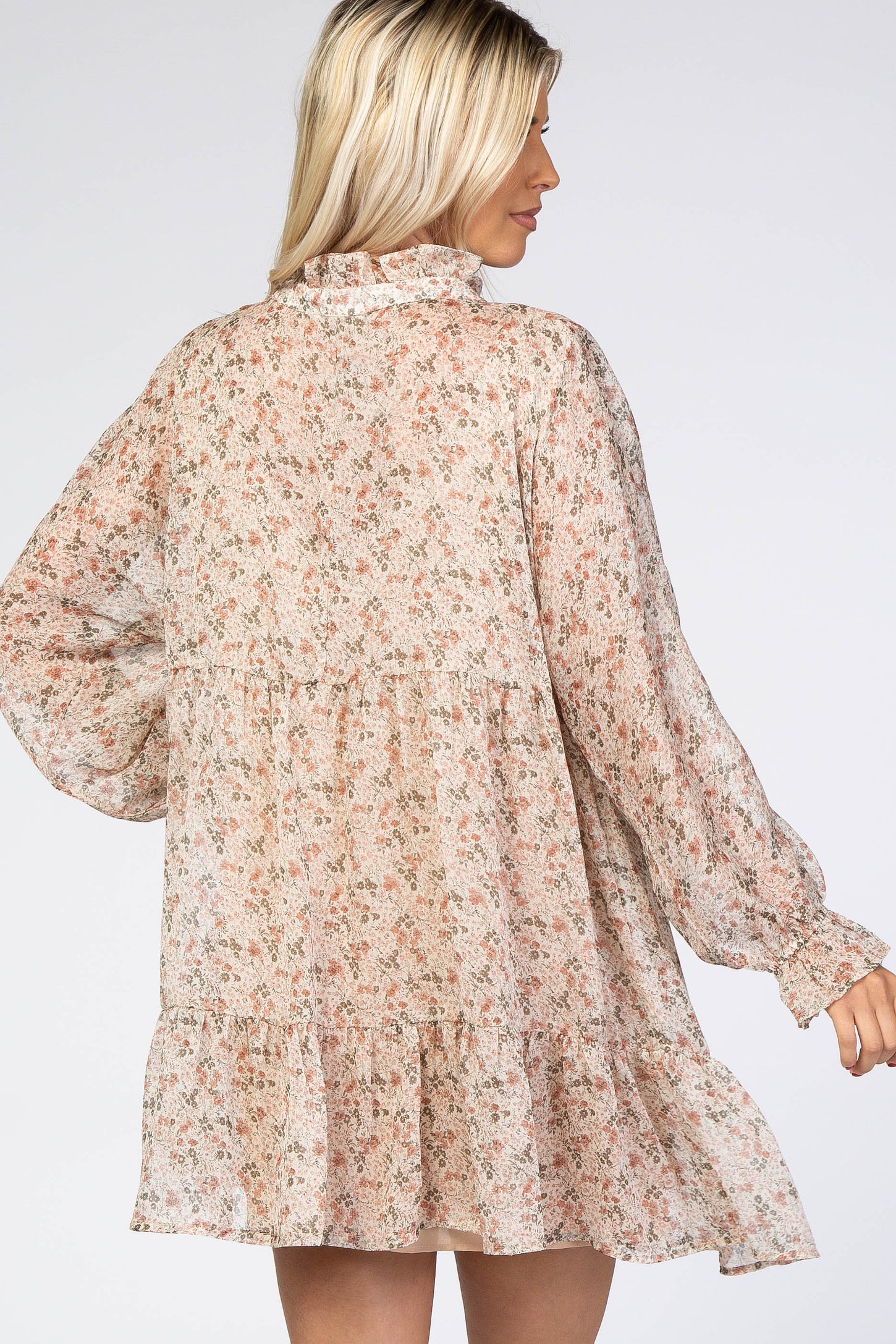 woman wearing a floral long sleeve tiered mini dress with a high neckline and relaxed fit from the back