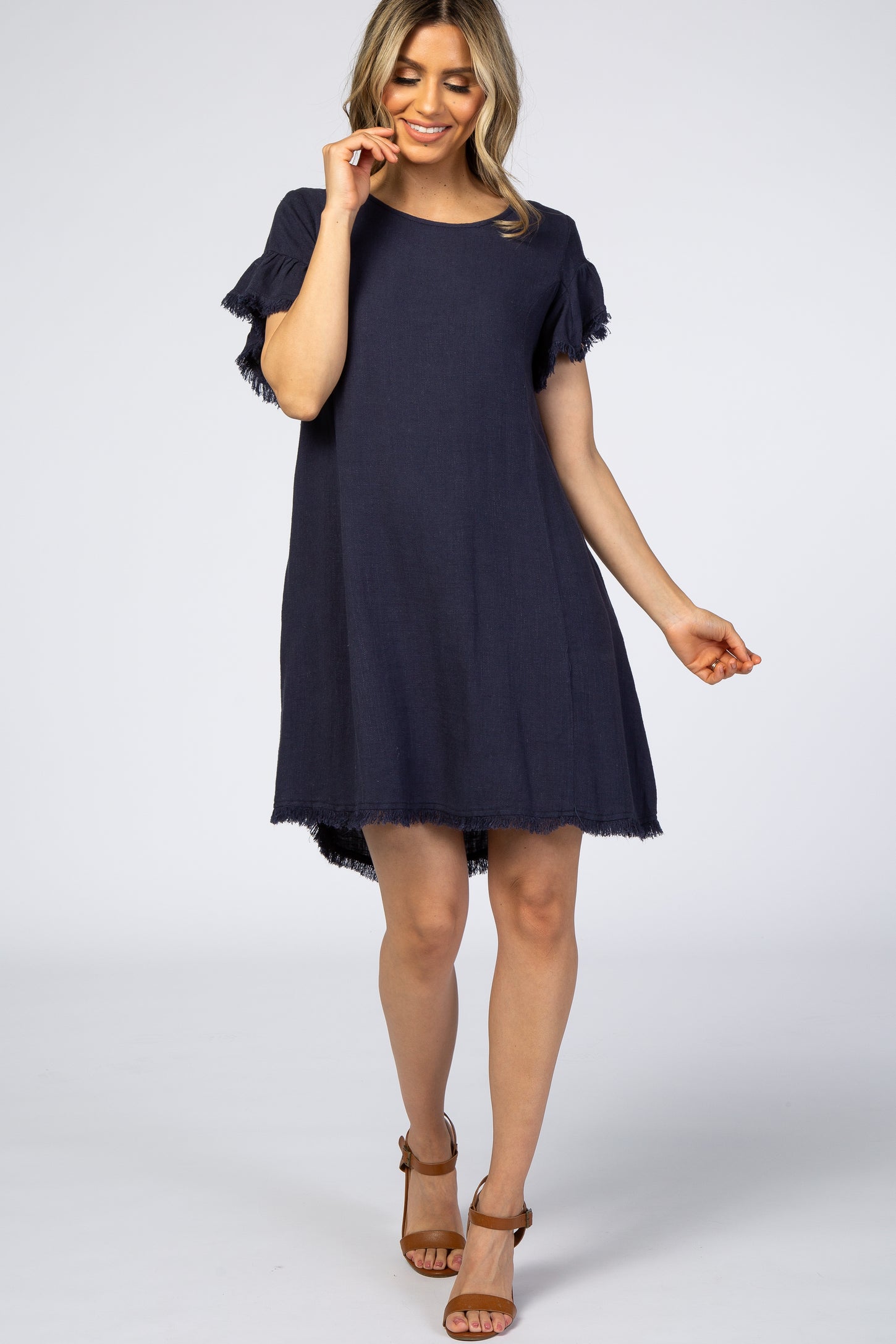 woman wearing a navy blue linen maternity shift dress with fringe trim and brown sandals