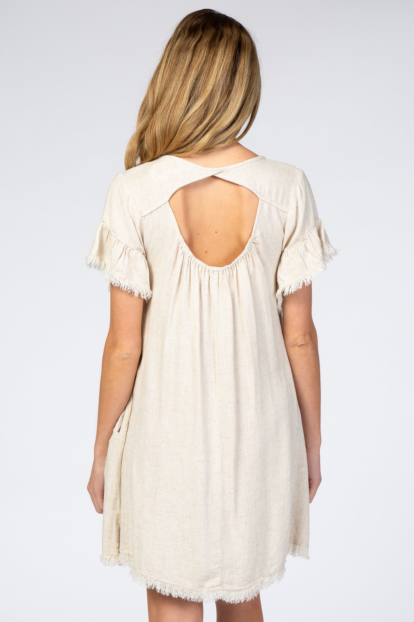 woman wearing a light beige maternity dress with a back cutout and frayed sleeves