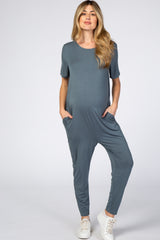 woman wearing a slate gray short sleeve maternity jumpsuit with pockets and a visible baby bump