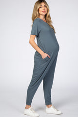 woman wearing a blue short sleeve maternity jumpsuit with pockets and a visible baby bump