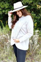 woman wearing a cream nursing hoodie and white wide brim hat standing outdoors in a field