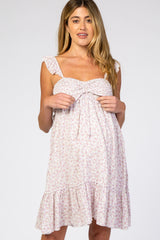 Pregnant woman wearing a white and purple floral maternity dress with ruffle sleeves and a tie front bust.