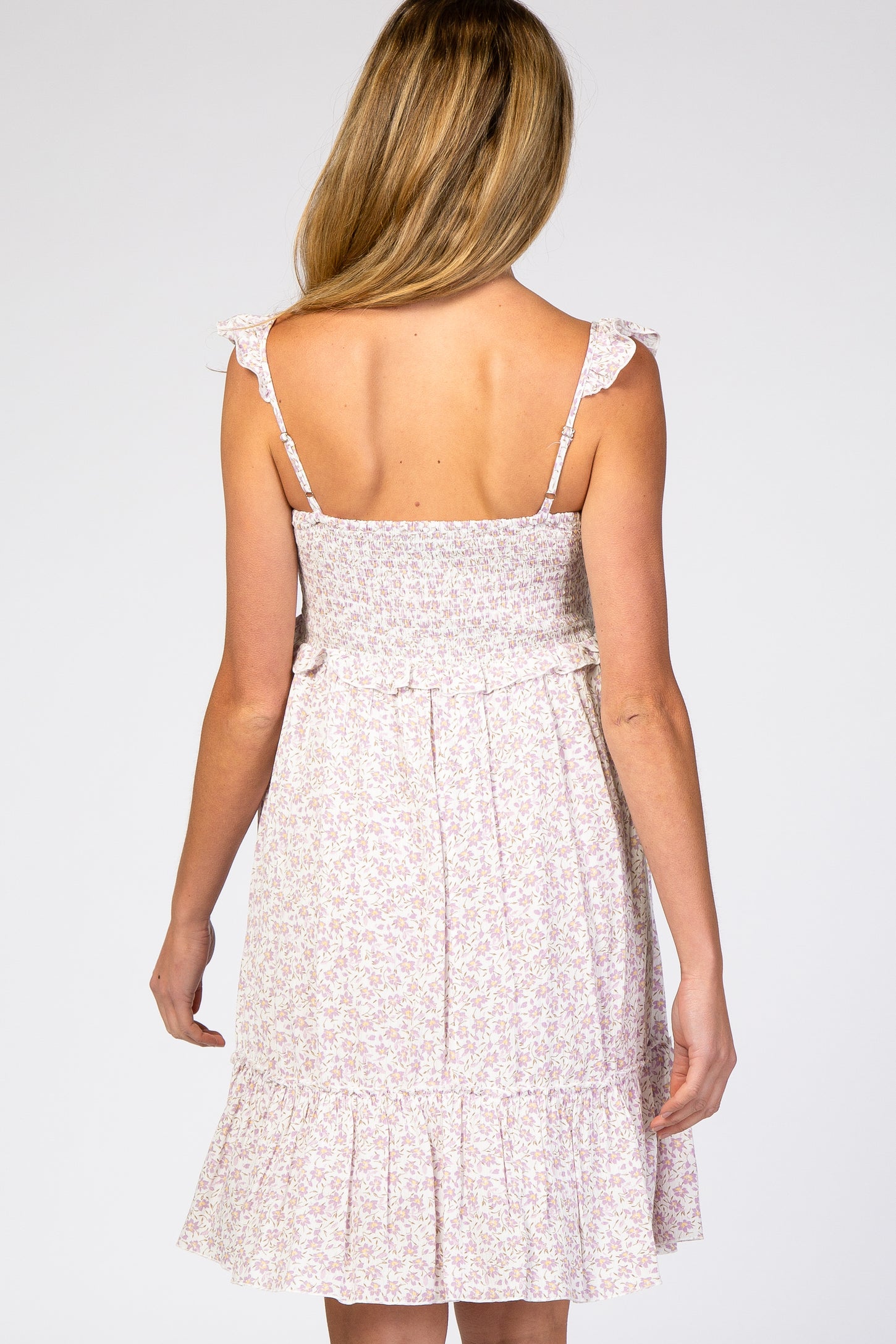 Back view of a woman wearing a purple floral smocked maternity dress with ruffle straps
