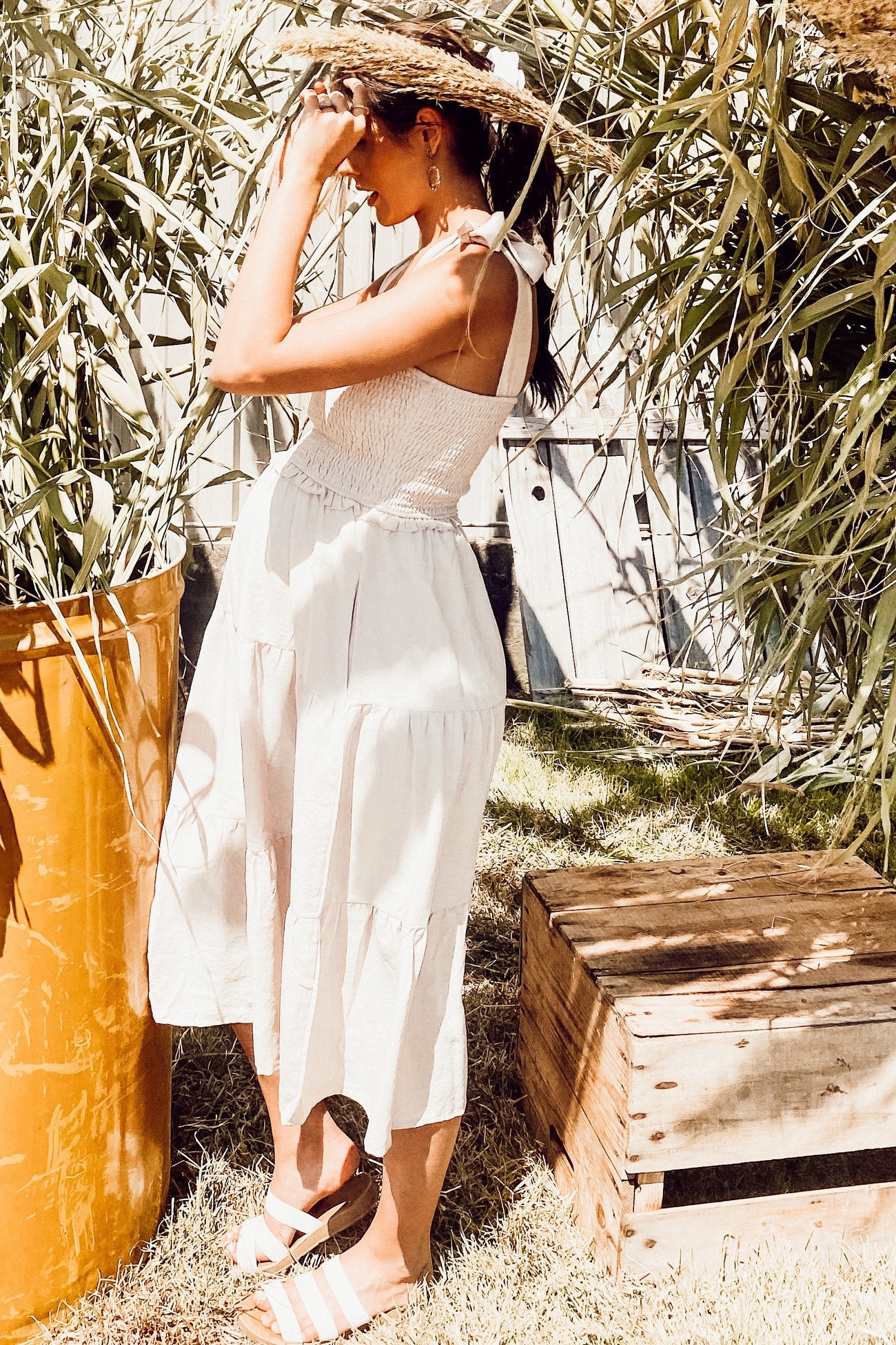 woman wearing a white maternity sundress with a smocked bodice and tiered skirt, standing outdoors with a baby bump visible