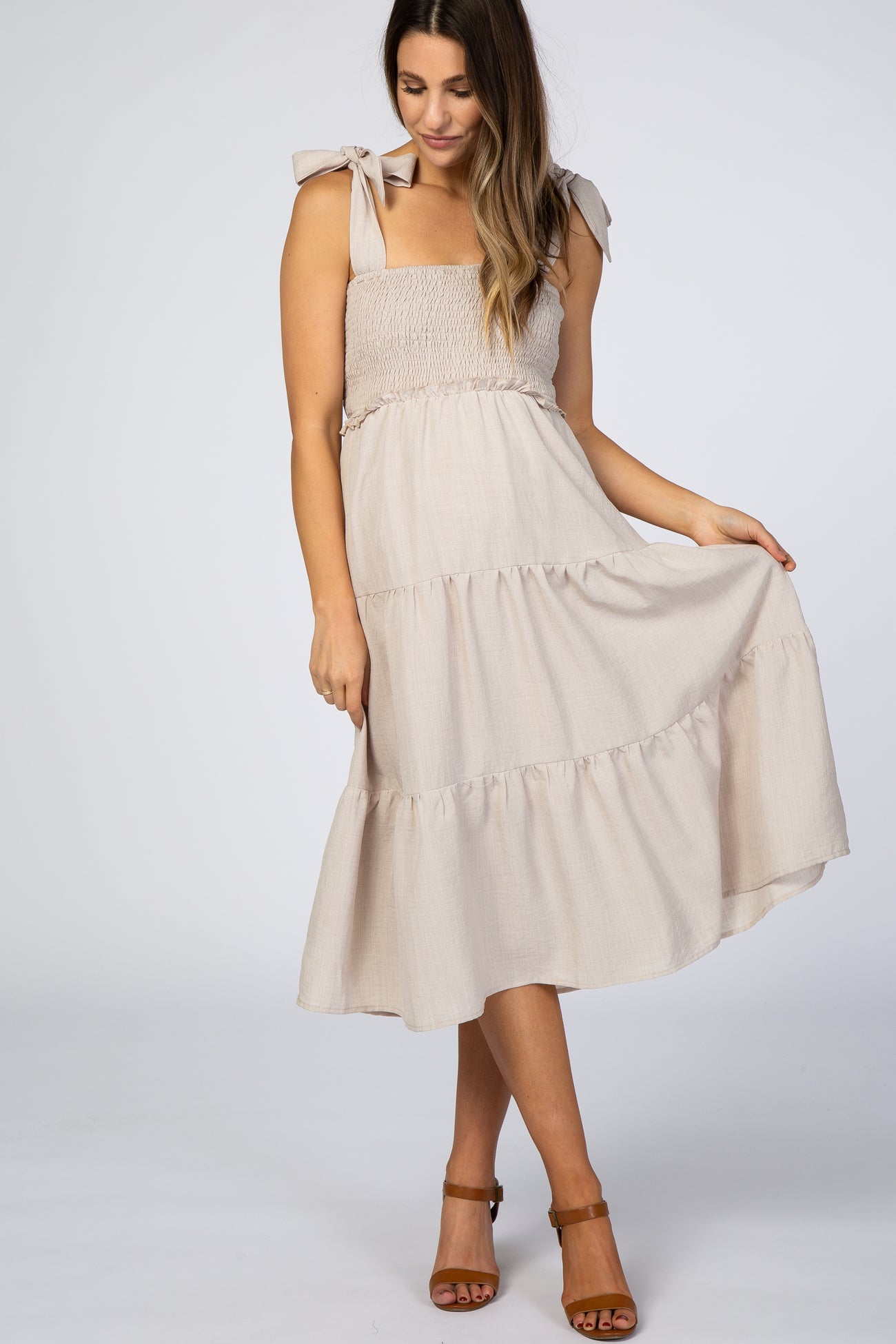 Woman wearing a beige smocked maternity midi dress with tie-straps and a tiered skirt