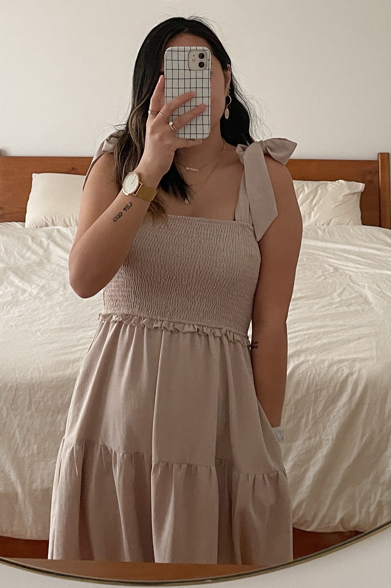 woman wearing a beige smocked midi dress with tie shoulder straps and a tiered skirt, mirror selfie in a bedroom