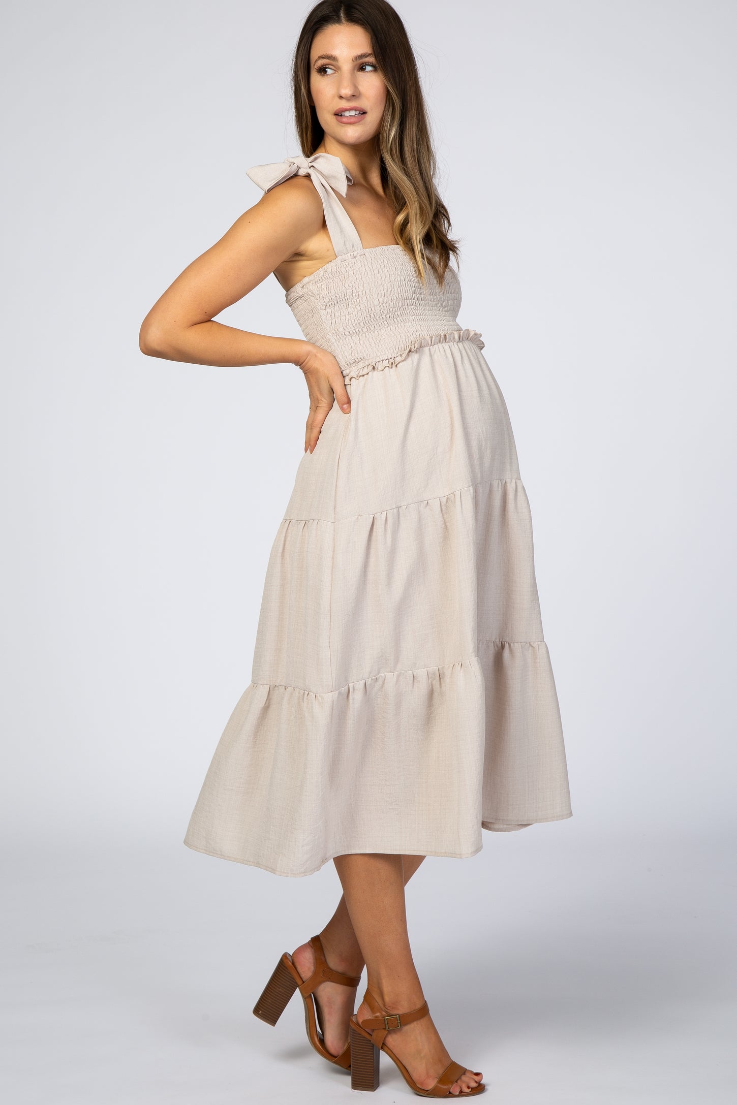 pregnant woman in beige smocked maternity midi dress with tie straps and tiered skirt
