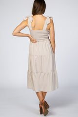 woman wearing a beige maternity dress with smocked bodice and tie straps, showing the back view