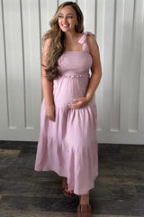 woman wearing a light pink maternity maxi dress with smocked bodice and ruffled straps, holding her baby bump