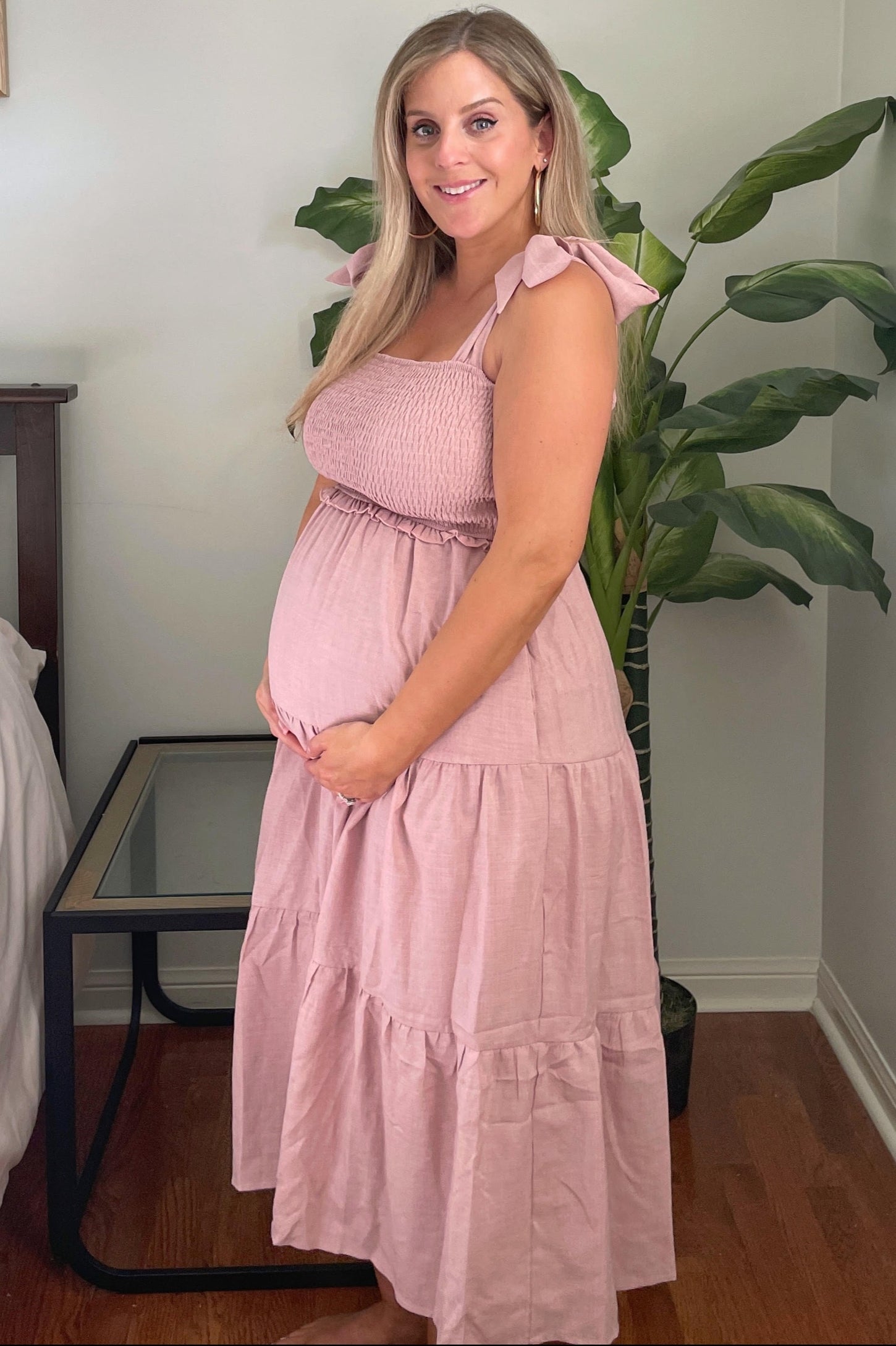 woman wearing a light pink maternity maxi dress with tie straps and a smocked bodice, holding her baby bump