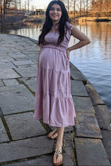 woman wearing a pink maternity maxi dress with flutter sleeves and a baby bump by the water