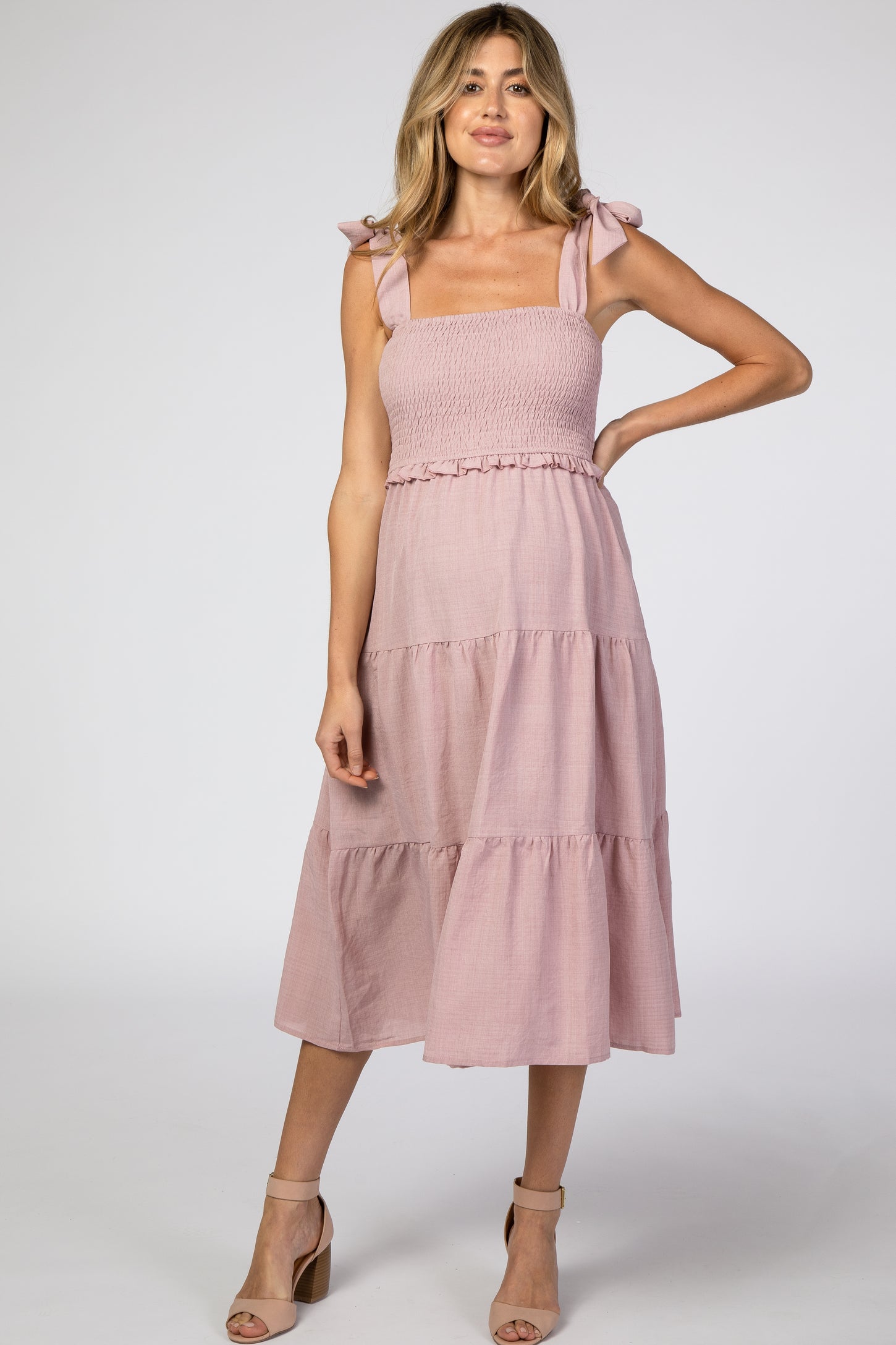 woman wearing a pink maternity dress with smocked bodice and tie straps, featuring a tiered skirt and no visible baby bump
