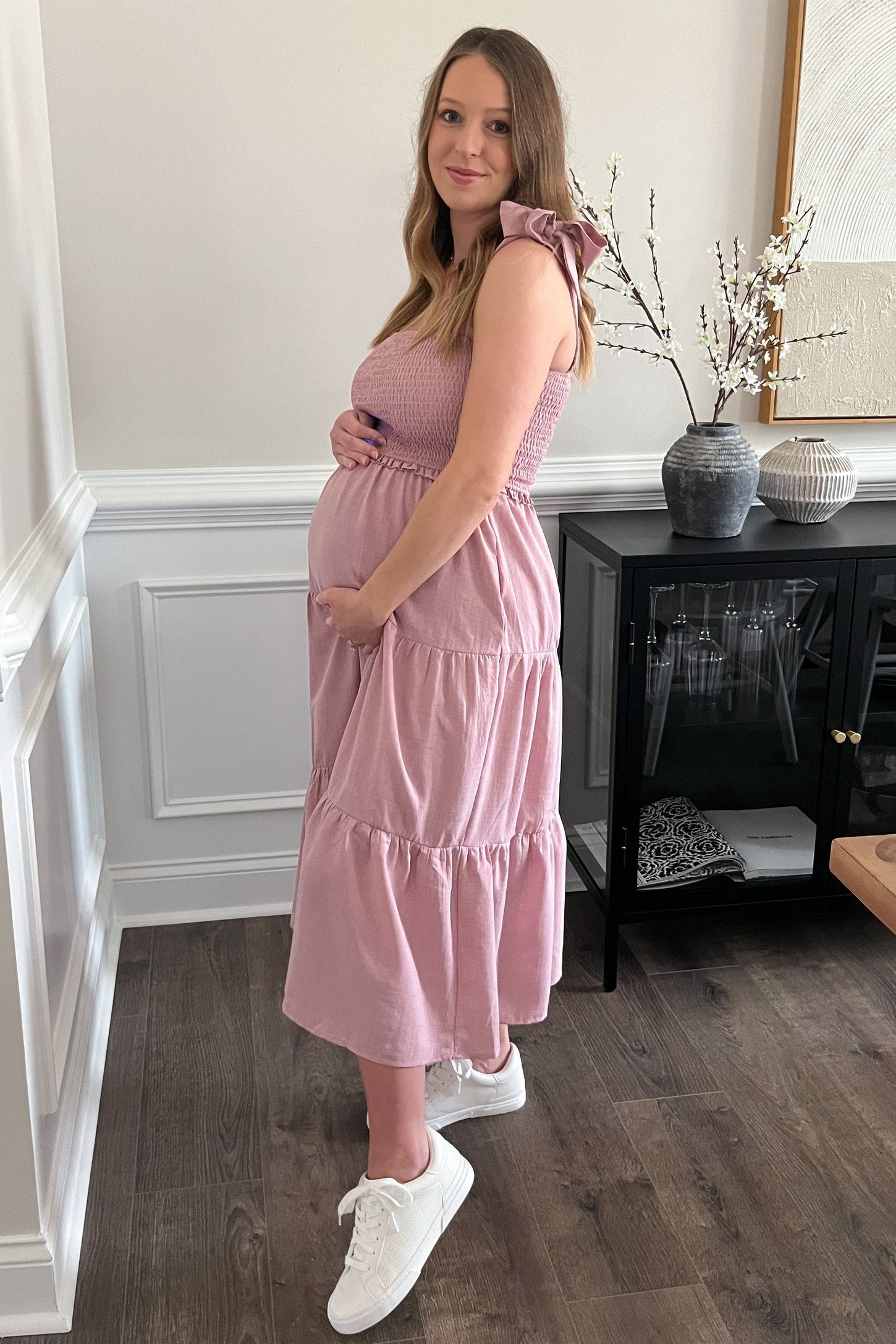 woman wearing a pink maternity dress with tiered design and shoulder ties, cradling her baby bump