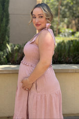 woman wearing a pink smocked maternity dress with ruffled straps, showing her baby bump while standing outdoors
