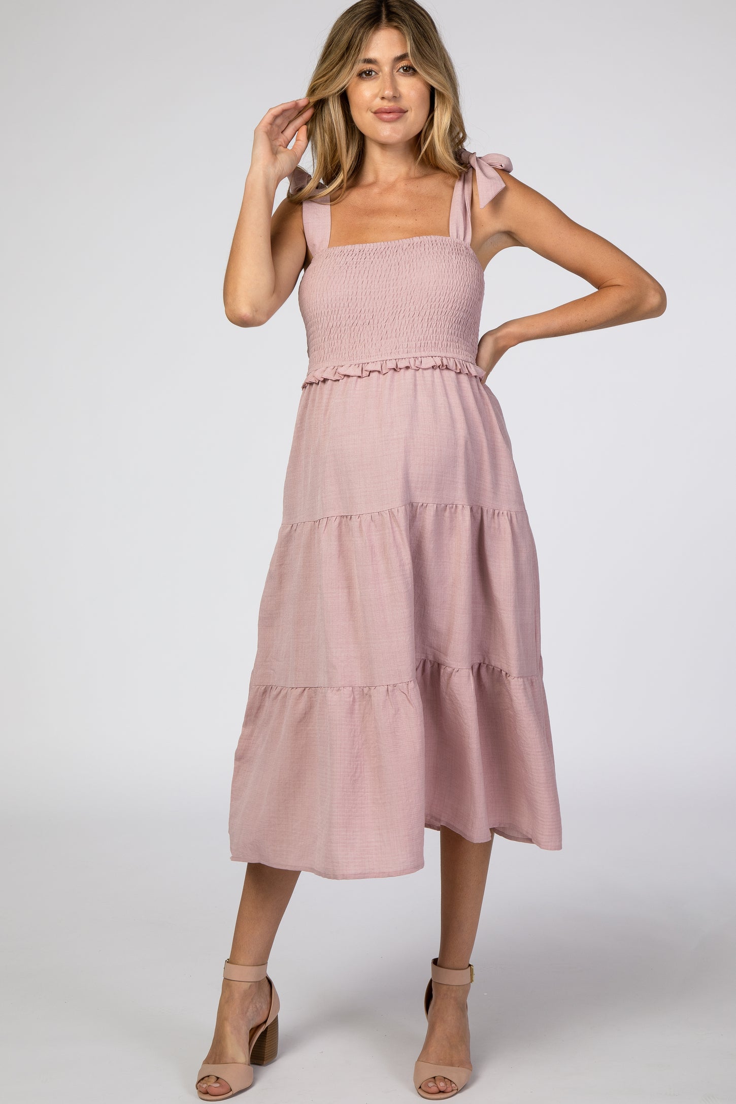 woman wearing a light pink maternity dress with tie straps and tiered skirt, showcasing her baby bump