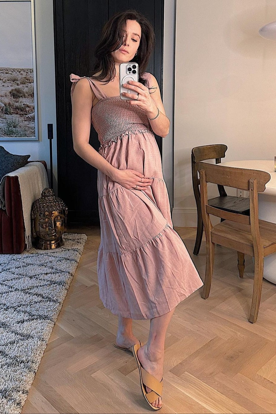 woman wearing a pink maternity midi dress with smocked bodice and tiered skirt, holding her baby bump