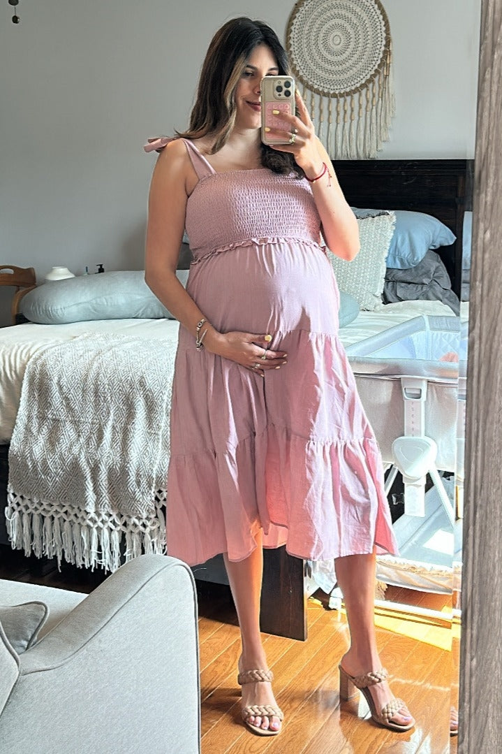 woman wearing a pink maternity sundress with smocked bodice and tiered skirt, showing her baby bump in a mirror selfie