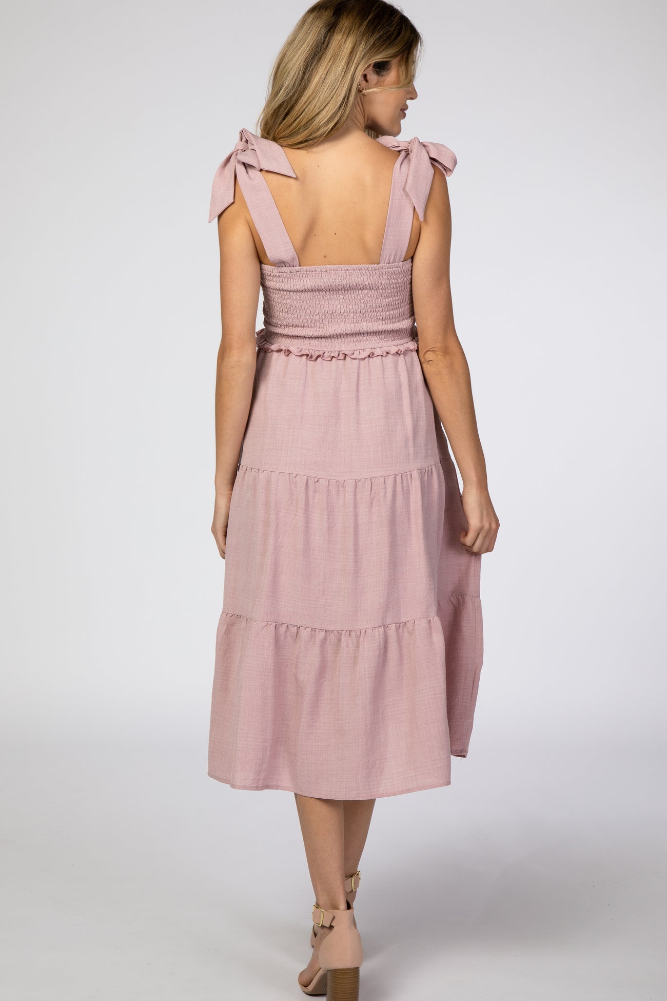 woman wearing a pink smocked maternity dress with tie straps and a tiered skirt, visible baby bump