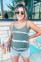smiling woman in green tie-dye tank top and sunglasses holding an iced coffee outside a cafe