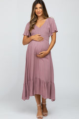 woman wearing a dusty rose maternity dress with short ruffled sleeves and a tiered skirt, holding her baby bump