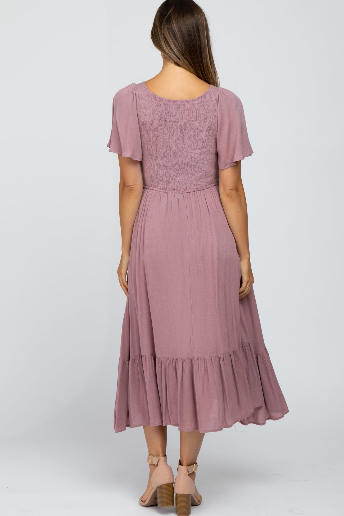 Back view of a woman wearing a mauve smocked midi dress with flutter sleeves and a tiered hem