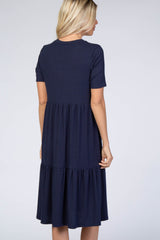 woman wearing a navy blue short sleeve tiered dress, showing a unique ribbed texture from the back