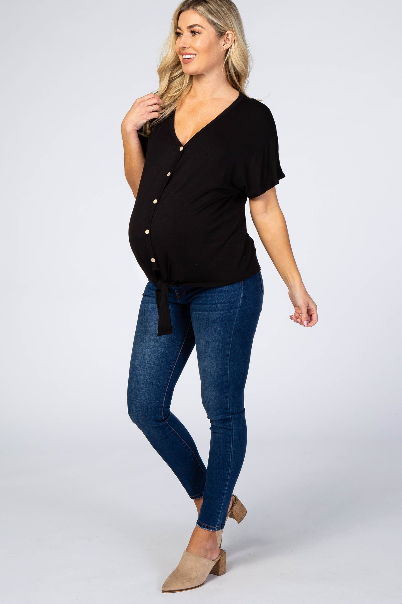 pregnant woman wearing black button down maternity top and blue skinny jeans with tan mules