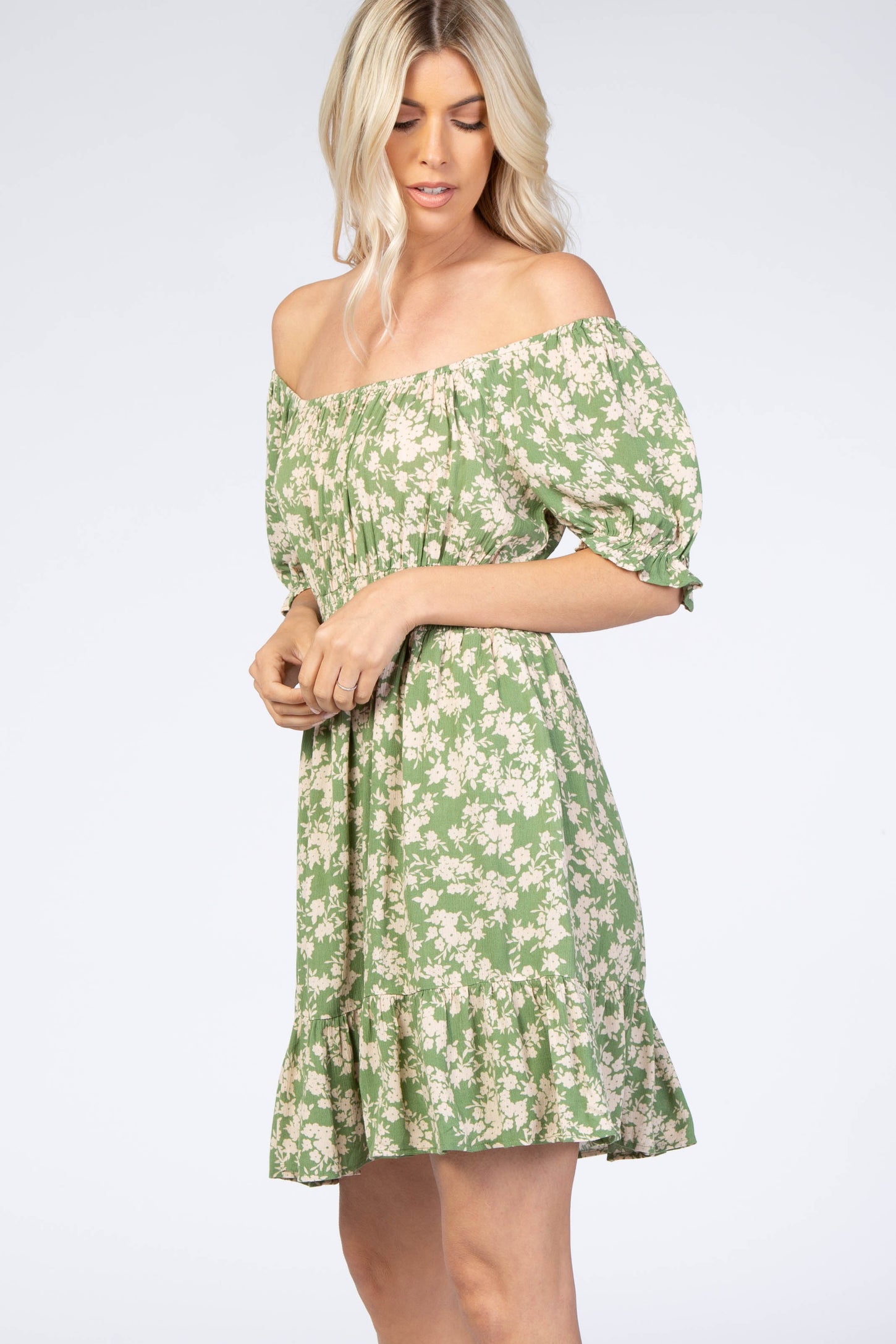 Woman wearing a green floral off-the-shoulder mini dress with puff sleeves and a ruffled hem.
