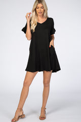 woman wearing a black short sleeve casual dress with a v-neck and pockets, standing against a white backdrop
