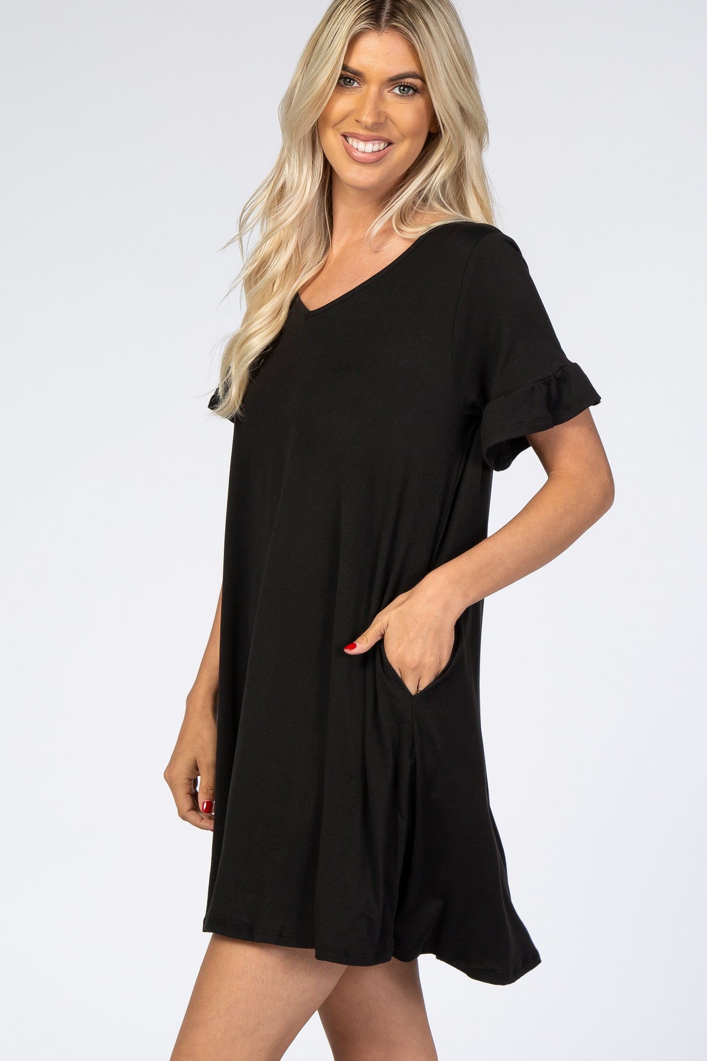 woman wearing a black short sleeve dress with ruffle sleeves and pockets, smiling at the camera
