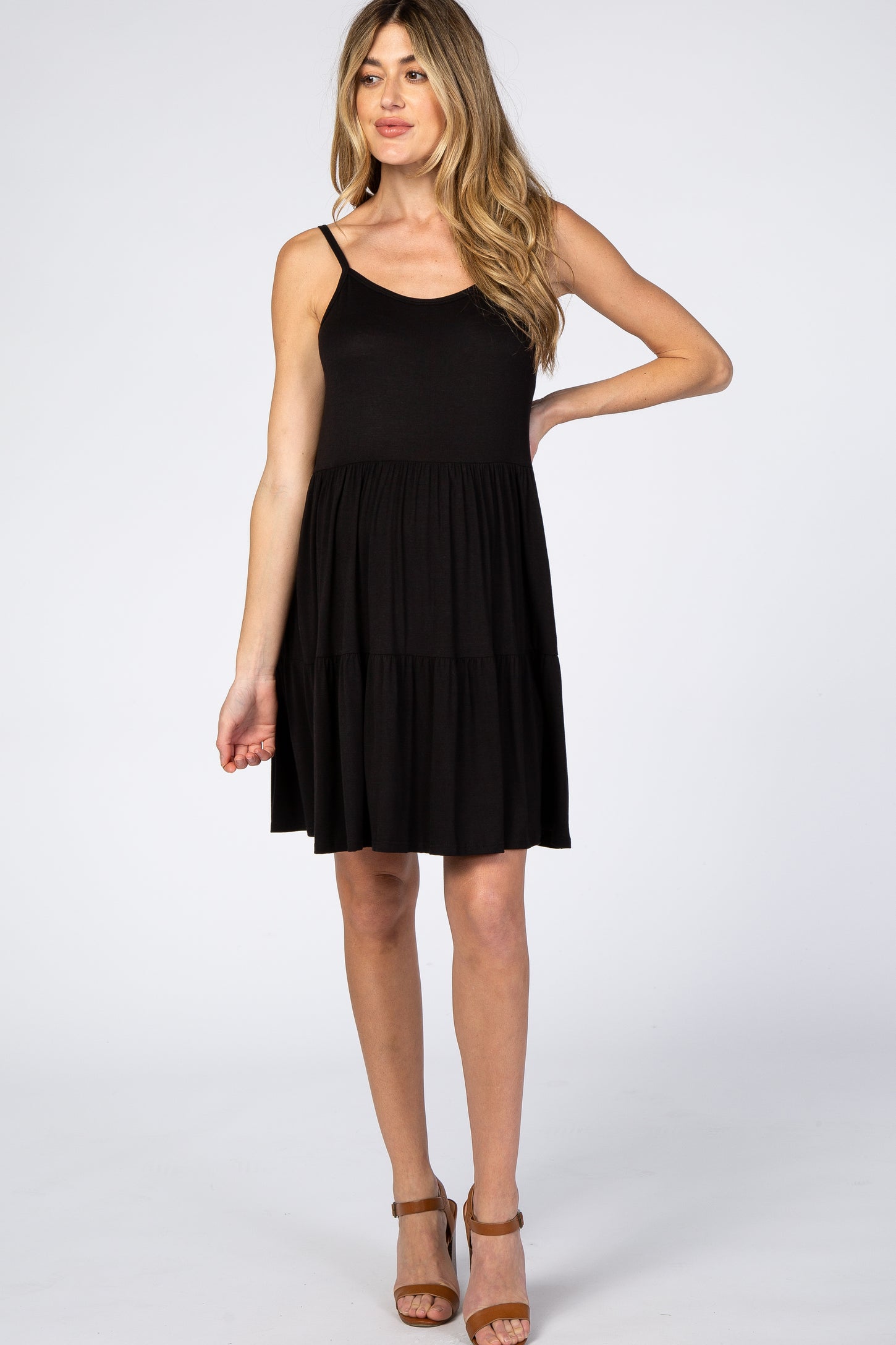 woman wearing a black sleeveless tiered maternity dress and brown strap heels against a white background