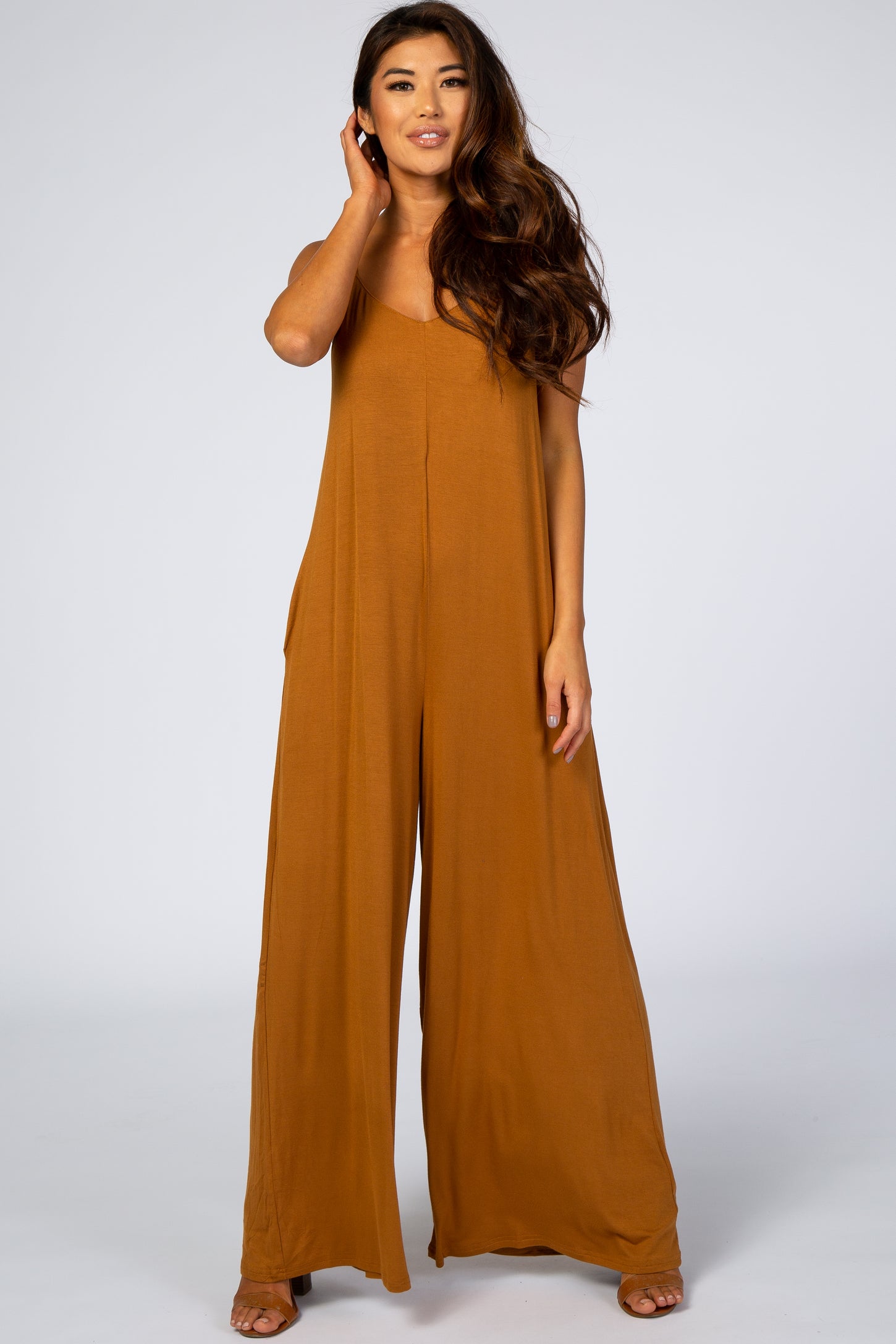 woman wearing a camel colored wide leg maternity jumpsuit with spaghetti straps and pockets