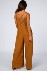 Back view of a woman wearing a camel-colored wide-leg jumpsuit with crisscross spaghetti straps
