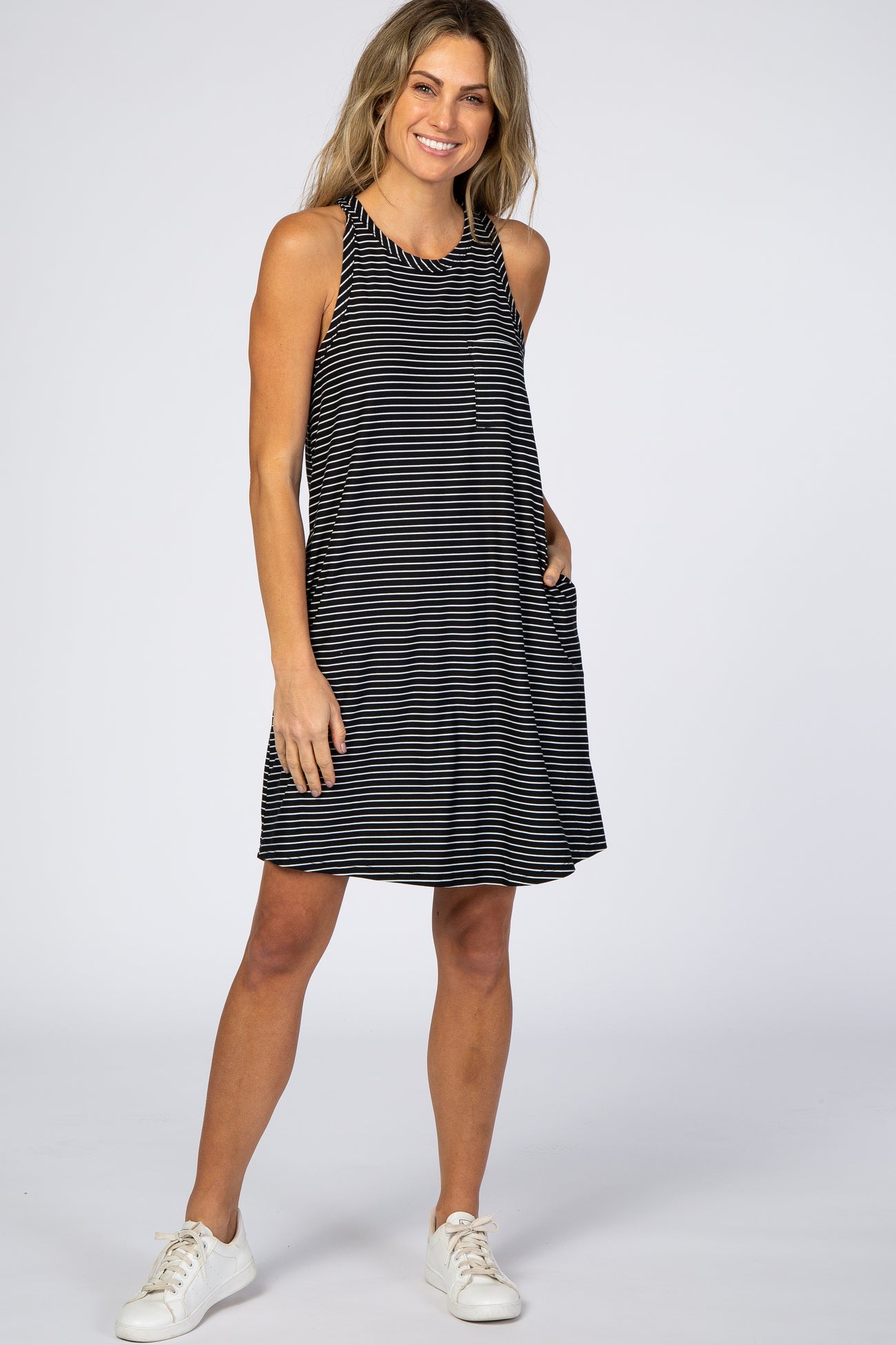 woman wearing a black and white striped sleeveless maternity dress with pockets and white sneakers