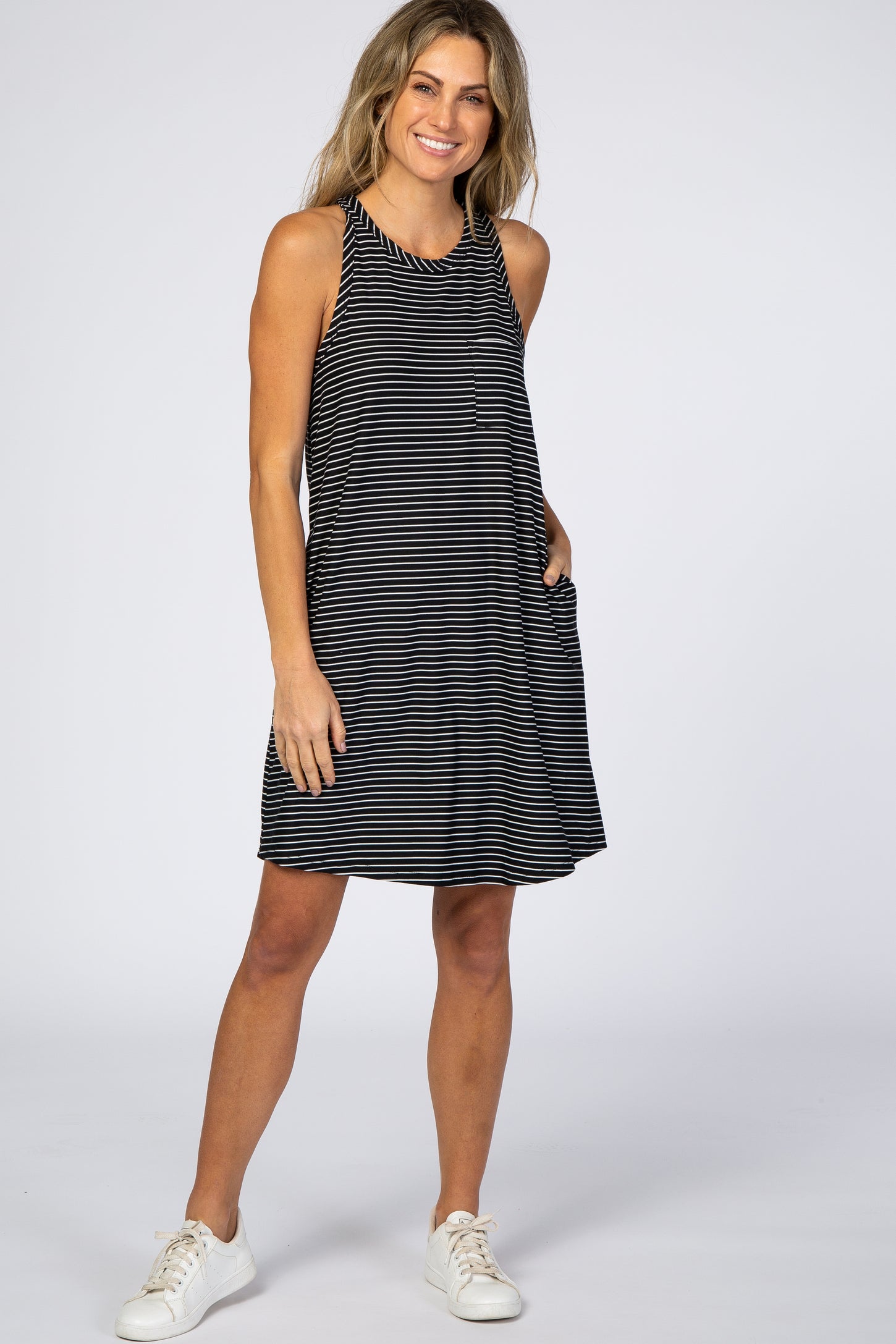 woman wearing a black and white striped sleeveless maternity dress with pockets and white sneakers