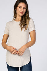 woman wearing a light beige short sleeve maternity top and gently holding her baby bump
