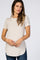 woman wearing a light beige short sleeve maternity top and gently holding her baby bump