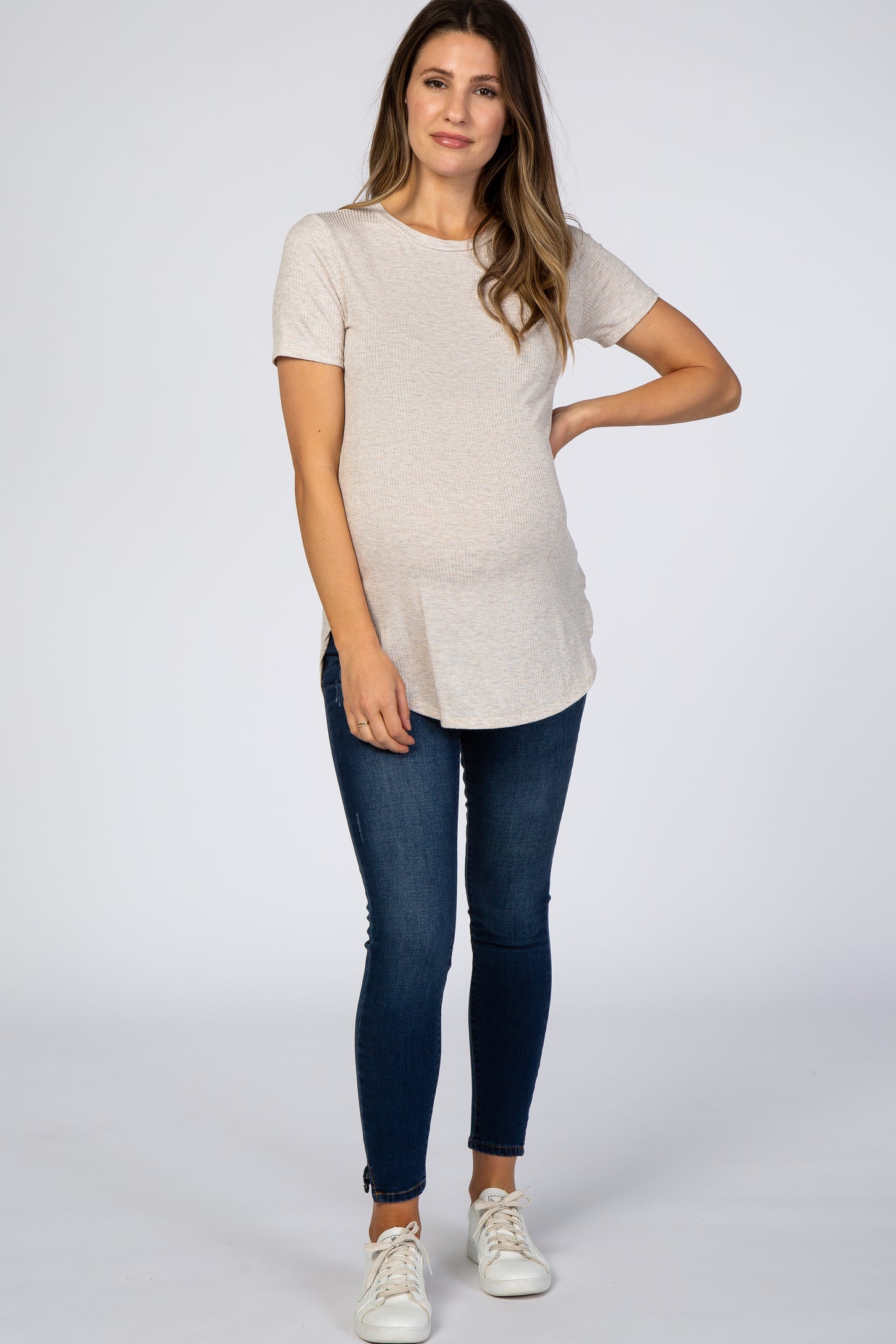 woman wearing a light beige short sleeve maternity top and dark skinny jeans, showing her baby bump
