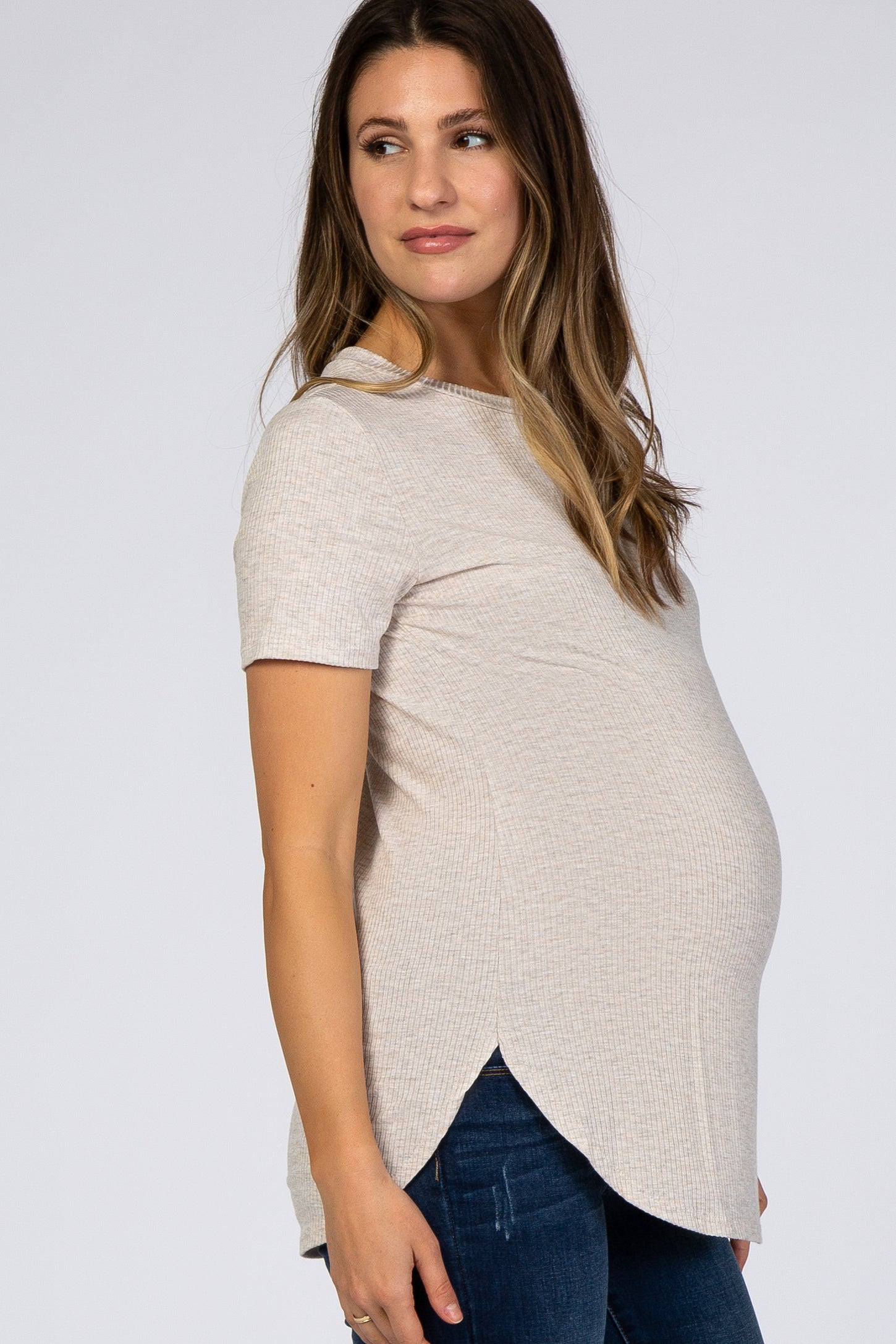 woman wearing a light beige short sleeve maternity top with a curved hem and a visible baby bump