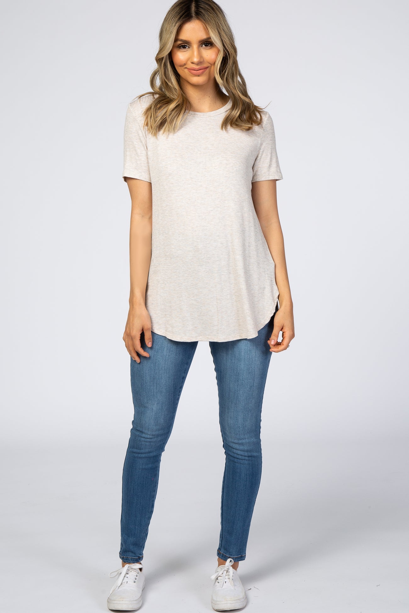 woman wearing a light beige short sleeve top with side slits and blue skinny jeans
