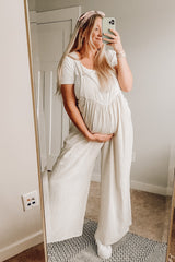 pregnant woman in white maternity overalls taking a mirror selfie while holding her baby bump