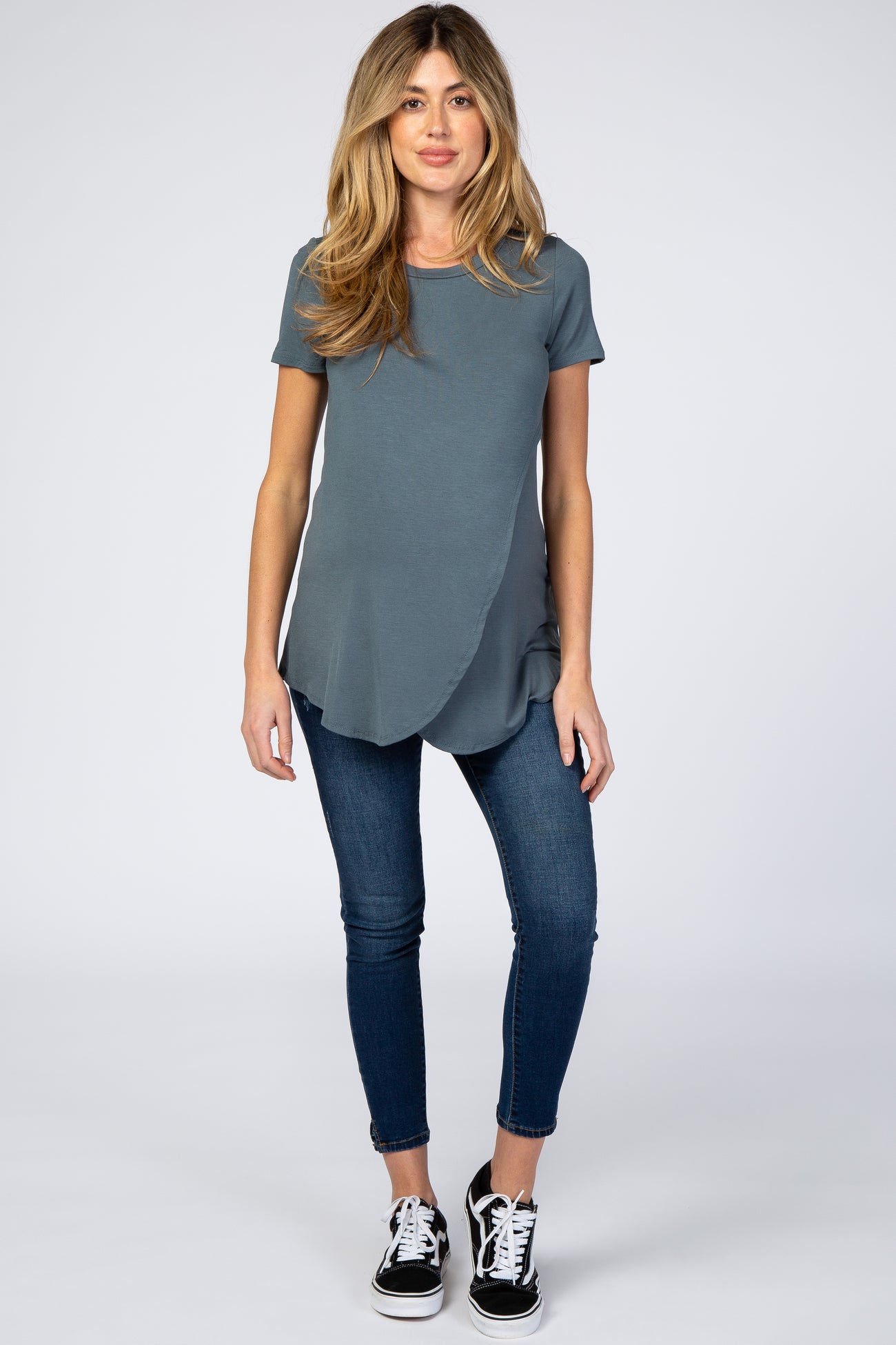 woman wearing a teal maternity top with a curved hem and short sleeves paired with skinny jeans