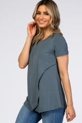 woman wearing a teal short sleeve top with a layered design, paired with denim jeans