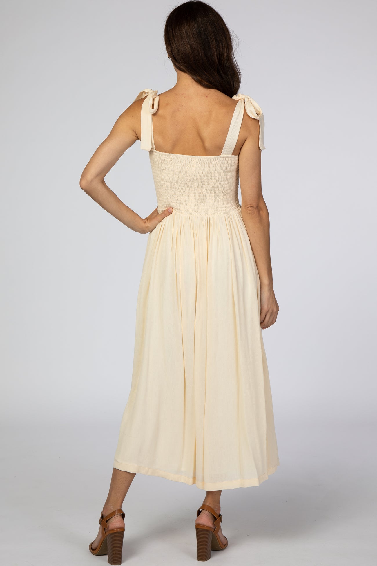 woman wearing a cream smocked back midi dress with tie straps and a flowy skirt