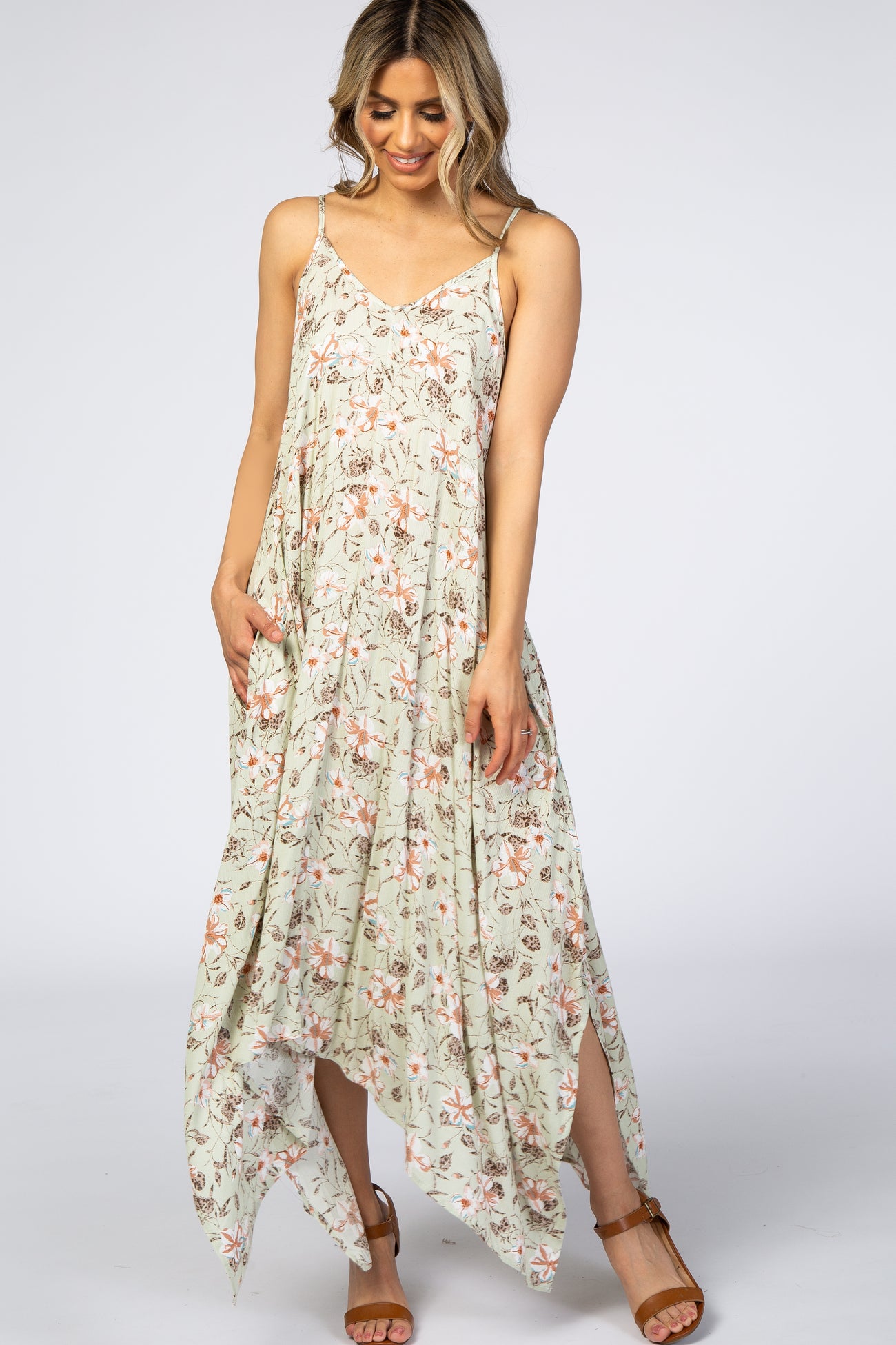 Woman wearing a sage green floral maternity maxi dress with a handkerchief hem and brown strappy sandals